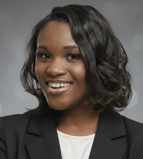 Professional headshot of a smiling woman with shoulder-length dark wavy hair wearing a black blazer over a white top