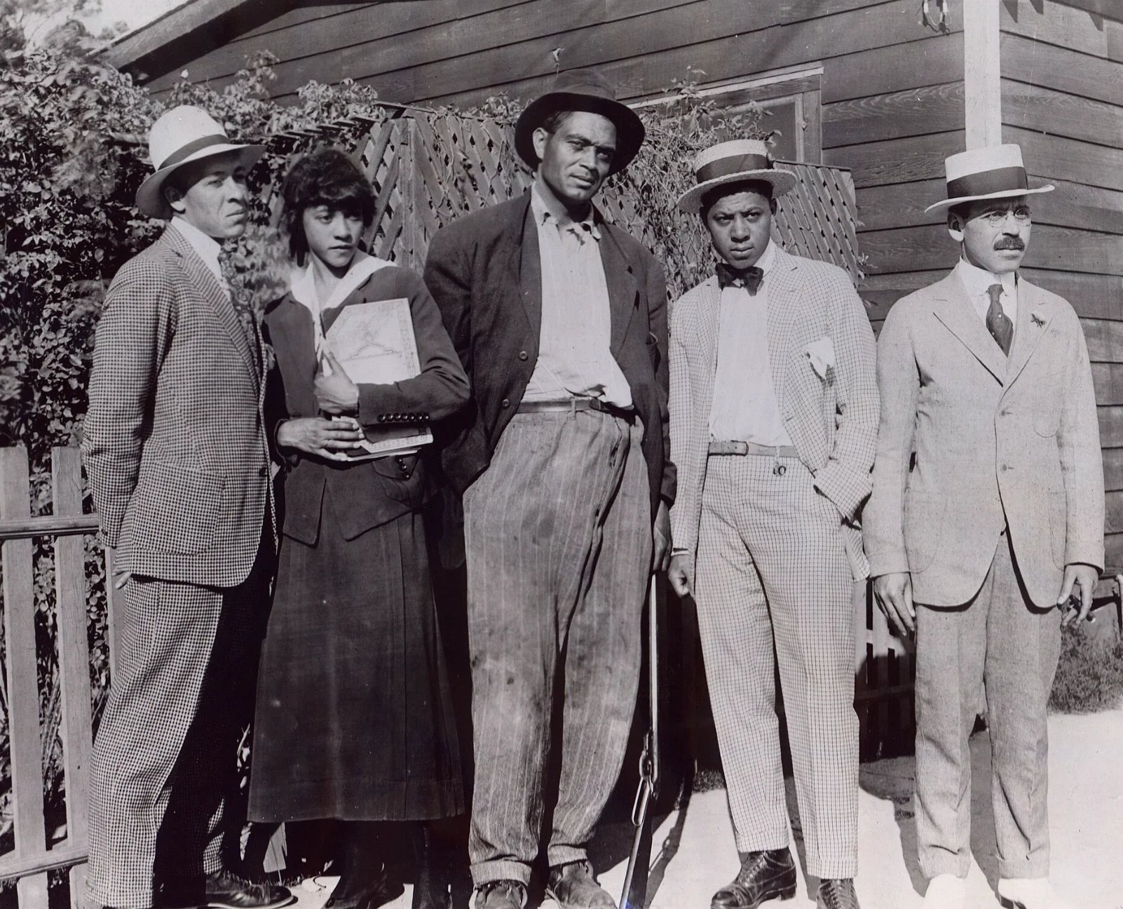 Five men in vintage suits and fedoras standing outside a house in a black and white photograph from the early 20th century