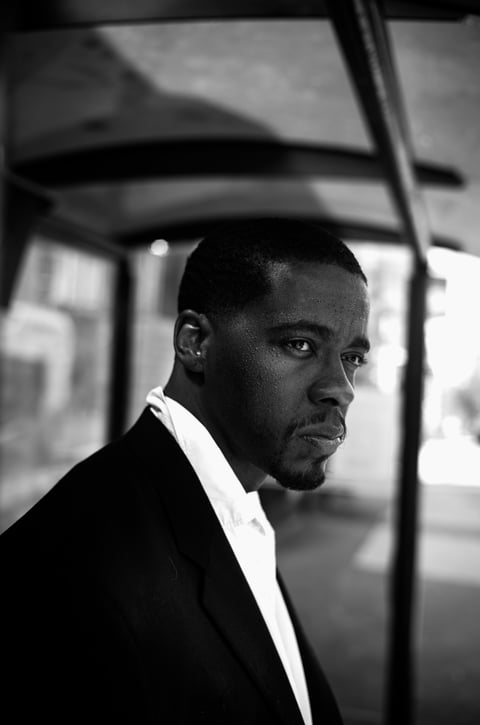 Black and white portrait of a man in formal attire looking over his shoulder inside a vehicle