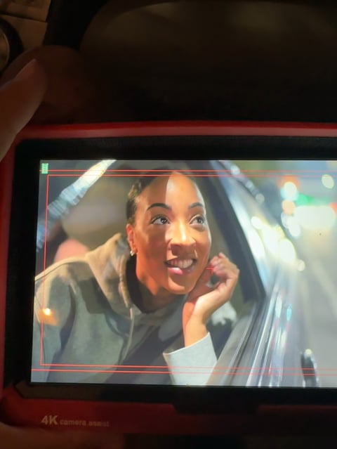 Woman smiling and looking upward through car window at night with city lights in background